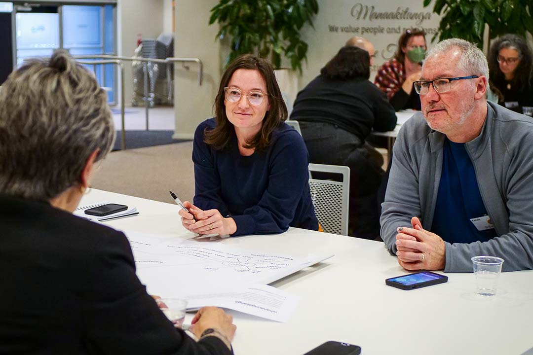Three people in conversation are seated at an office table.