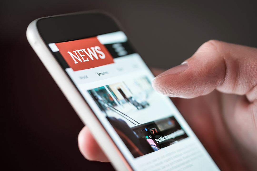 A phone in a persons hand. The phone is open on a news application.