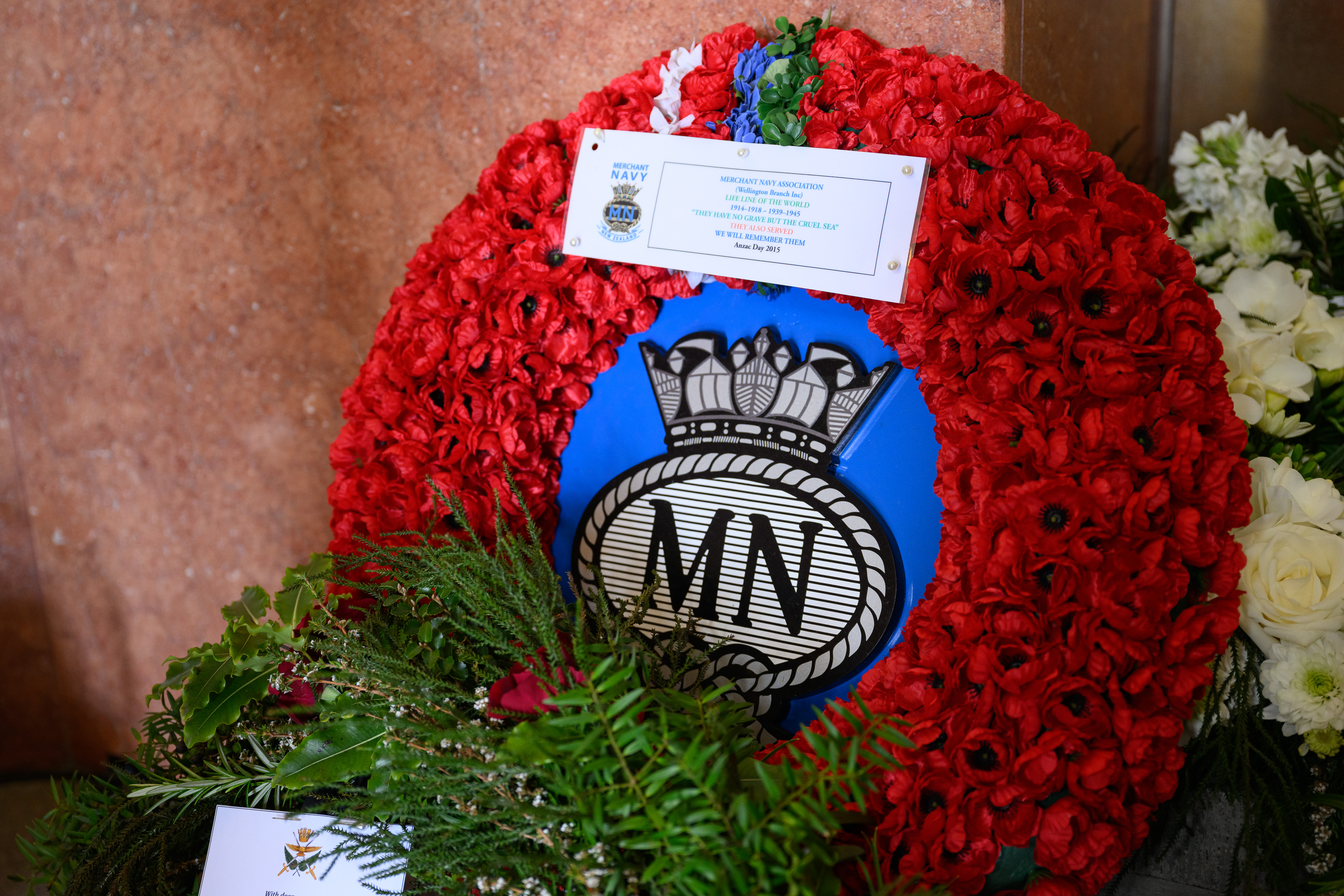 Wreath of red flowers with Merchant Navy insignia in the centre.