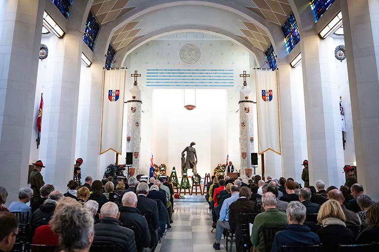 The inside of the Hall of Memories, rows of people seated facing a statue of a mother and children.