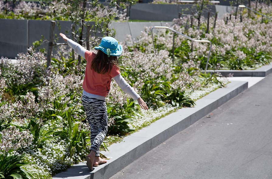 A child balancing on a low concrete ledge next to planted flowers at Pukeahu