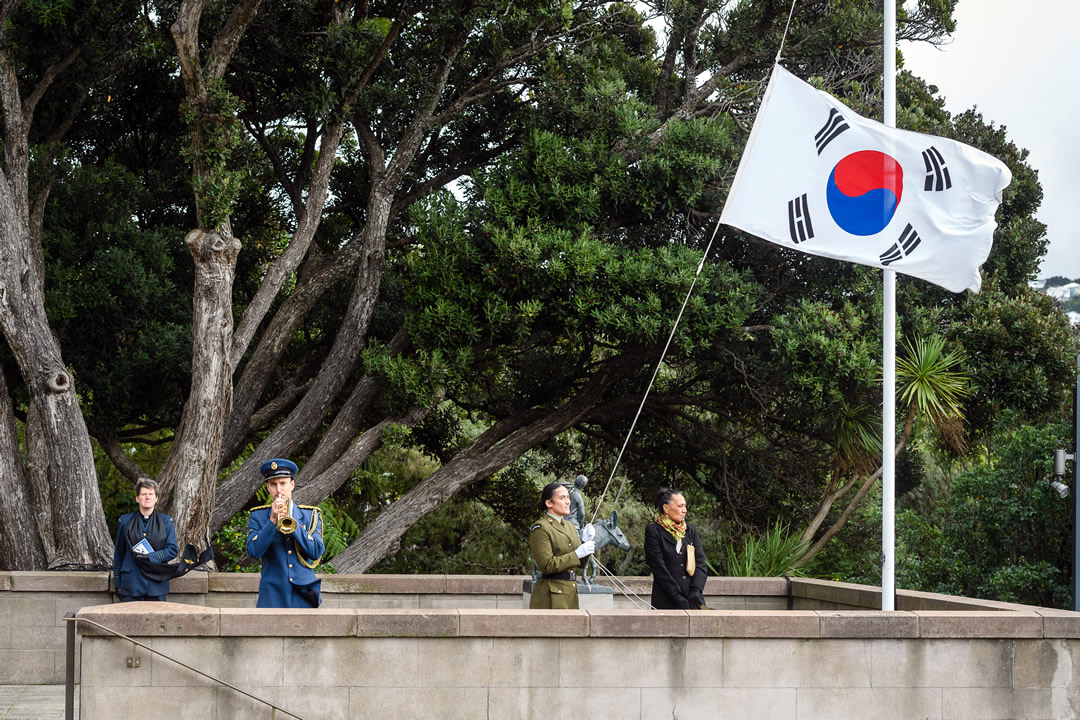 A person in a New Zealand military uniform lowers the Korean flag at Pukeahu park. 