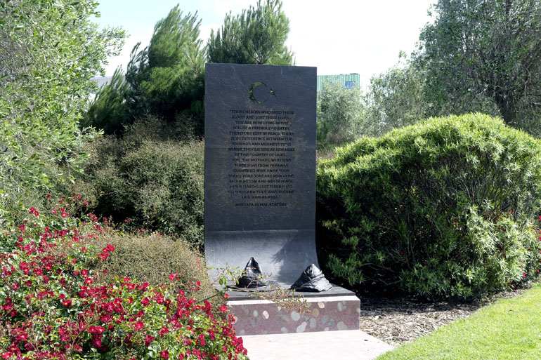 A metal plaque with two soldiers hats at the base surrounded by trees.