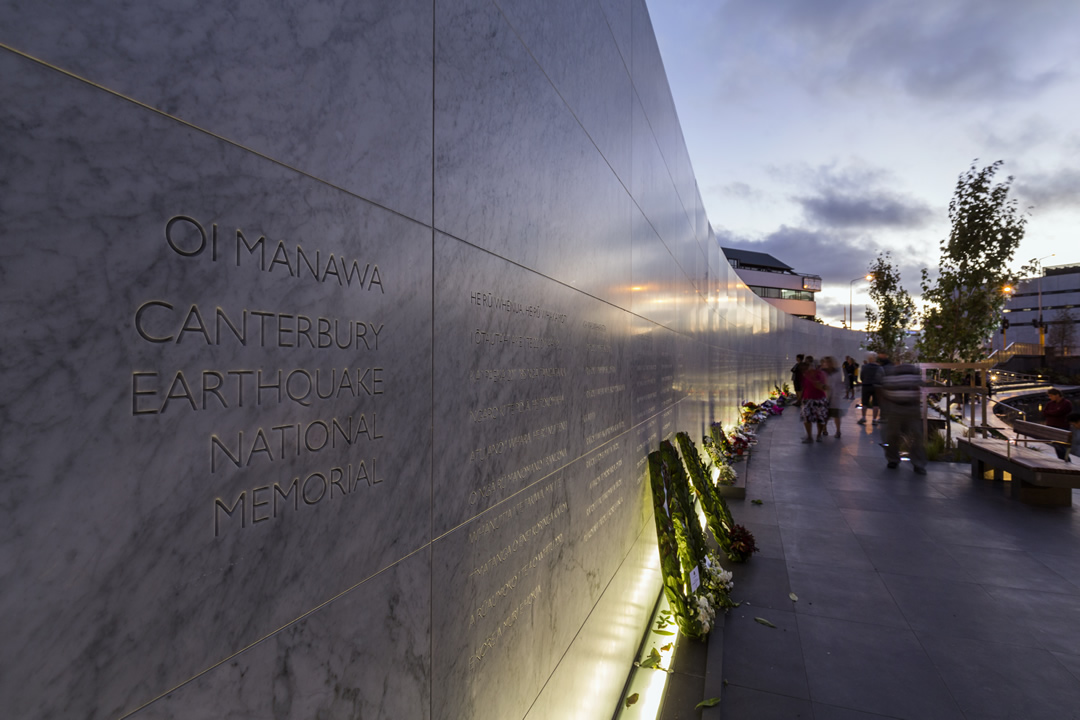 Memorial with wreaths laid against it and a few people looking