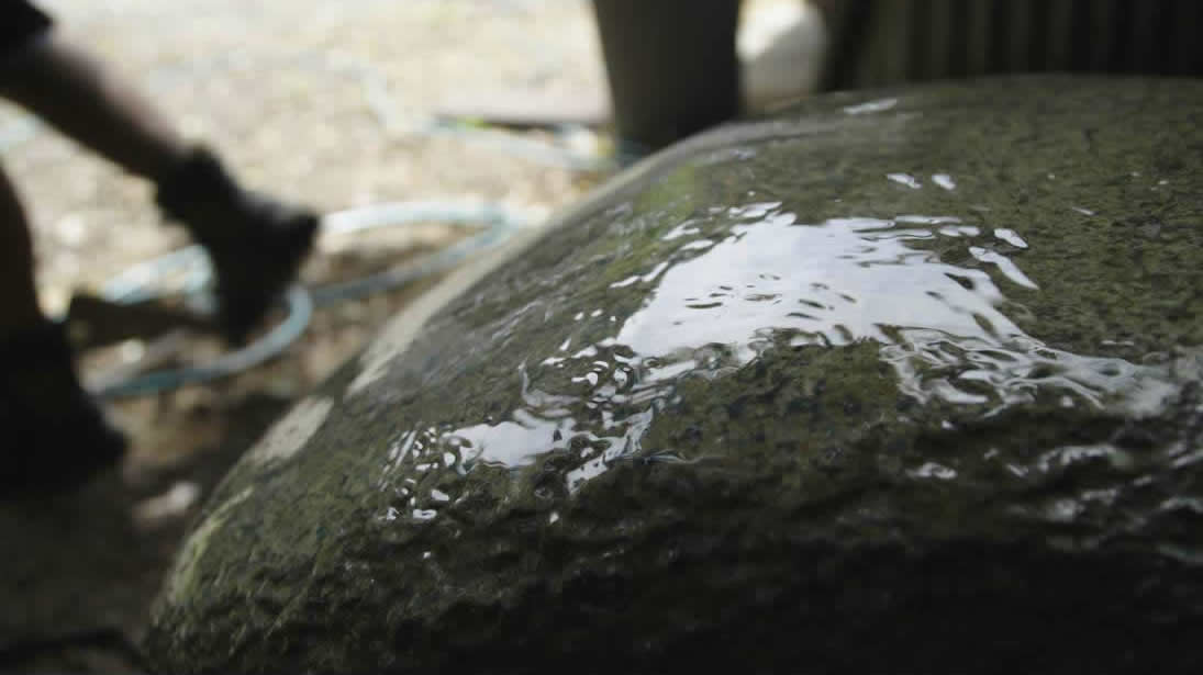 Large green boulder with water running over it
