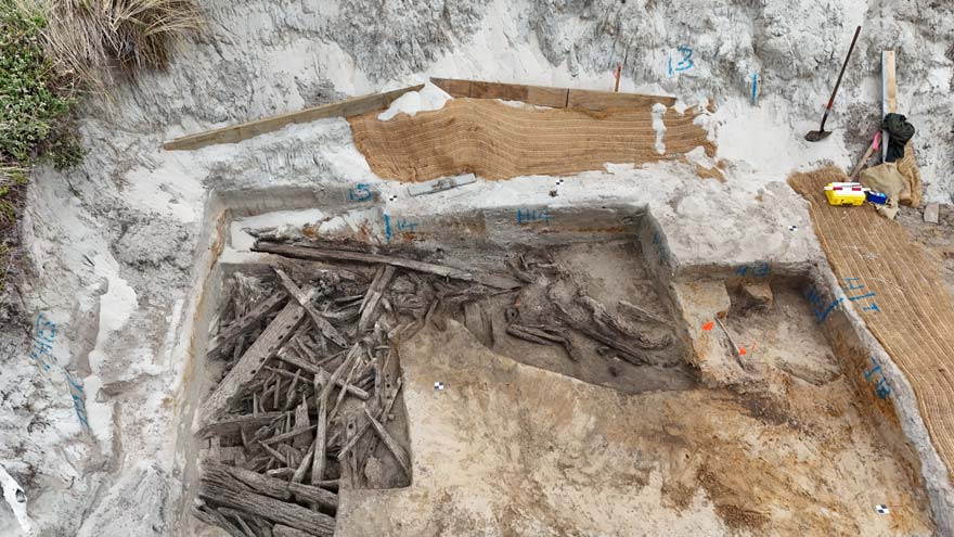 Wooden pieces of different shapes sitting inside a rectangular hole cut into the sand. 