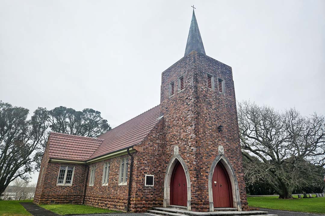Red brick church with prominent spire set against green lawn and trees