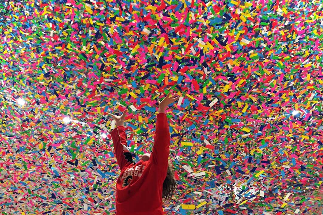 Child holding up their arms to a low ceiling filled with colourful confetti-like scraps