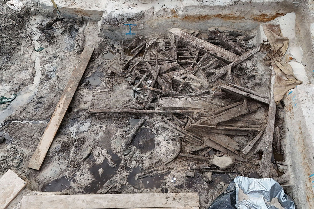 Jumble of different shaped wooden fragments in pit and covered in light layer of sand