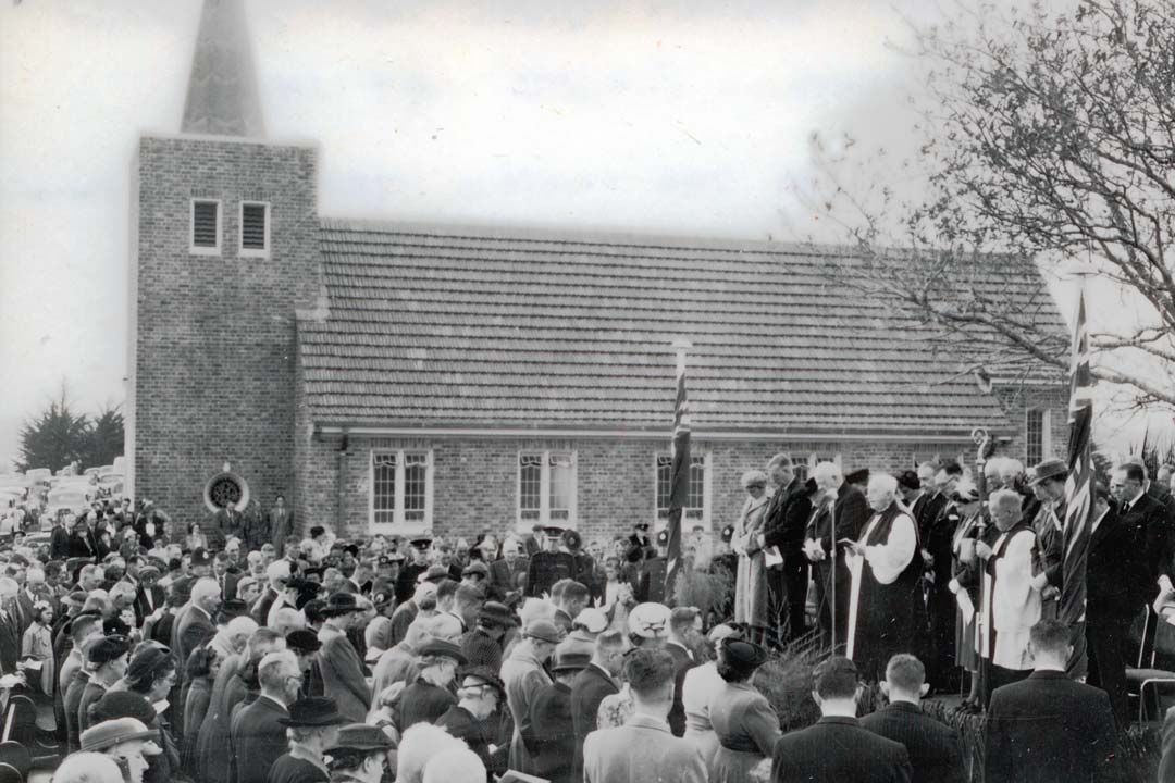 A black and white photo of a dense crowd gathered outside a brick church.