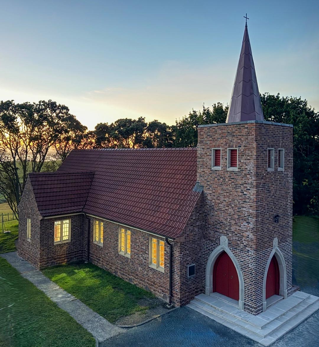 An orange brick church with red joinery against a sunset sky.