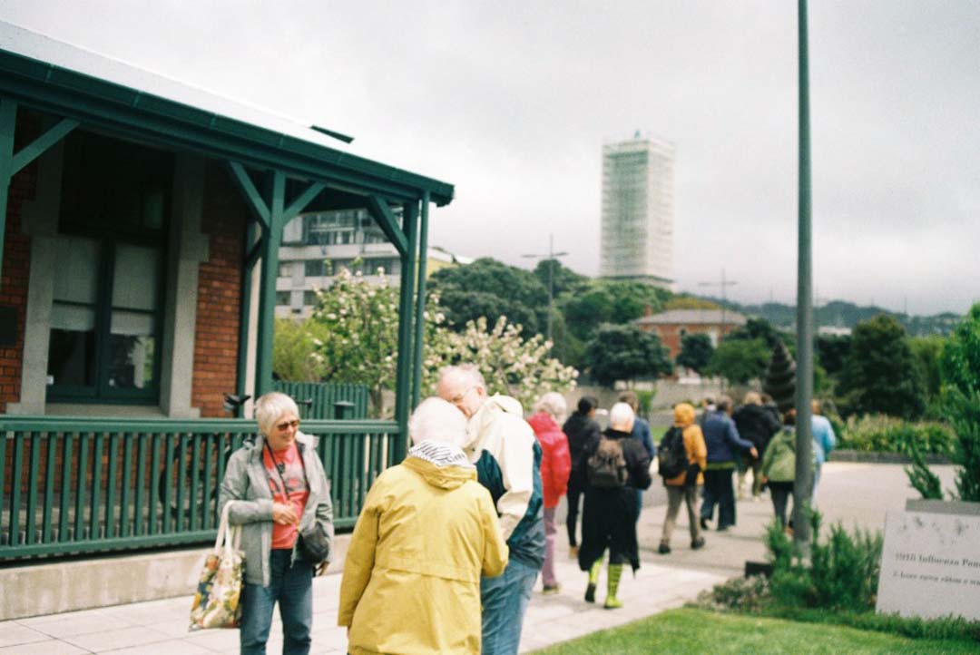 Walking group of people gathered around Pukeahu education centre, a villa with green balcony.