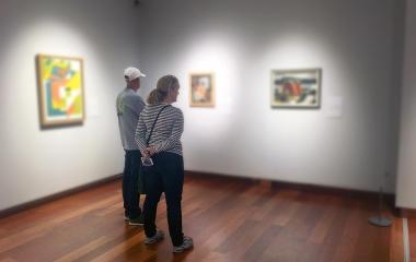 Two people looking at three paintings hung on a white gallery wall.