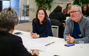 Three people in conversation are seated at an office table.