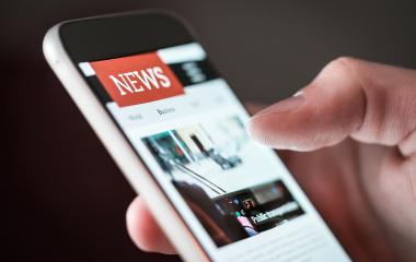 A phone in a persons hand. The phone is open on a news application.