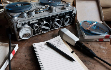 A tape recorder and microphone on a desk next to a writers pad and pen.
