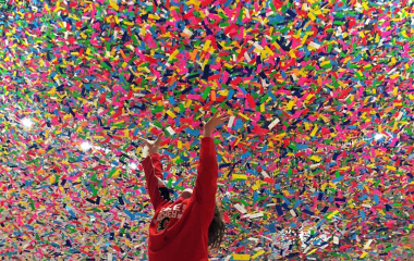 Child holding up their arms to a low ceiling filled with colourful confetti-like scraps