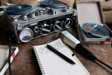 A tape recorder and microphone on a desk next to a writers pad and pen.