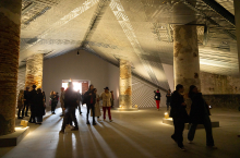 Visitors wandering around inside a modern whare-type building with light shining through slats in the roof