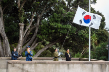 Four people standing outside the Carillon next to a flagpole flying the Korean flag