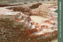 A pile of brick ruins lie in a circular pattern. On the far right hand side a green banner reads 'Pukeahu National War Memorial Park'.