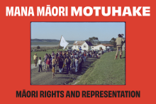 Red poster with large, bold white text reading ‘Mana Māori Motuhake’. A centred colour film photo shows people walking down a gravel road, led by a man carrying a white flag. Black text underneath reads ‘Māori rights and representation’.