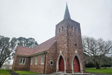 Red brick church with prominent spire set against green lawn and trees