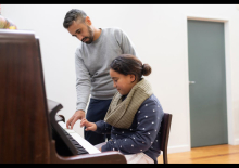 Child being shown how to play piano by adult